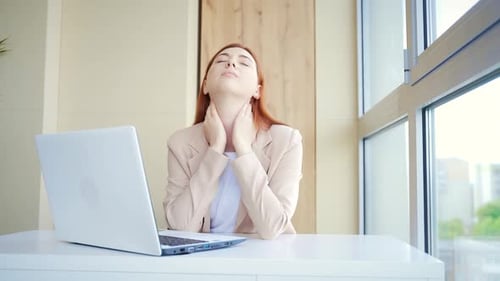 Close-up portrait of a young red-haired woman suffering from a severe headache at work in workplace.