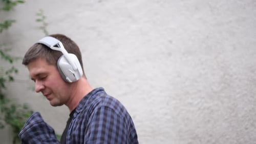 Jovem de camisa xadrez azul e camiseta preta ouve música com grandes fones de ouvido brancos e