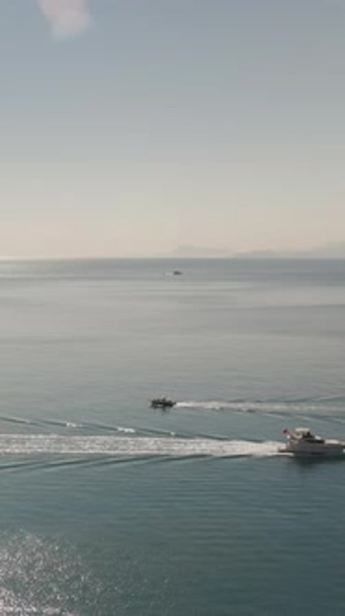 Two boats in the sea are sailing towards each other. Sun and mountains, top view. Vertical video Soc