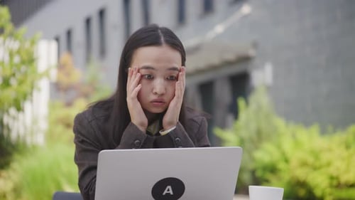 Asian Woman Reading Bad News on Her Laptop Upset Businesswoman Using Laptop Sitting Outside