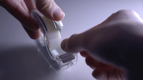 Hands Of A Woman Pulling Tape From A Transparent Scotch Tape Dispenser. - close up shot