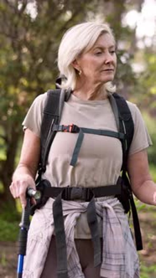 Mature woman, hiking and backpack with walking sticks in forest for adventure or outdoor journey