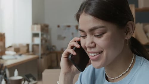 Close-up of Positive Young Woman Having Phone Conversation in Storage Room