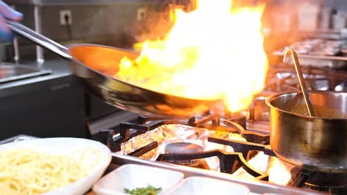 Nahaufnahme eines Restaurantkochs, der in der Restaurantküche brennendes Essen zubereitet