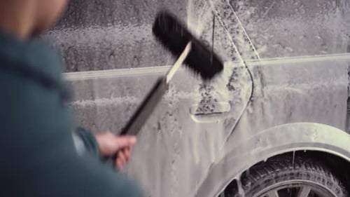 Person holding water pressure washer with brush, touchless car wash