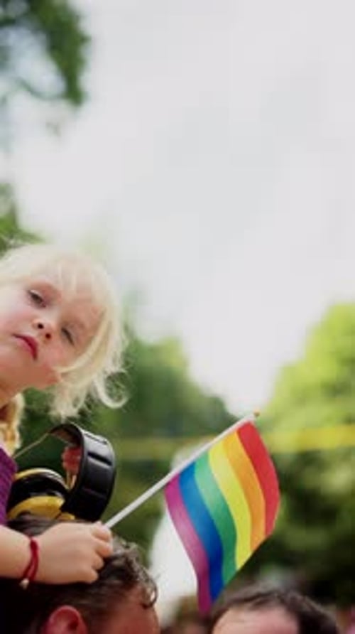 Child Carried at Outdoor Pride Event Waving Rainbow Flag