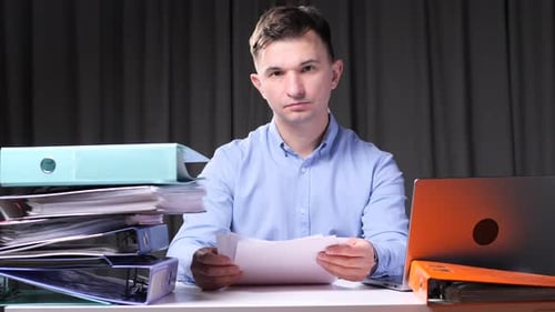 Office Worker Examining Documents at Desk with Laptop and Binders