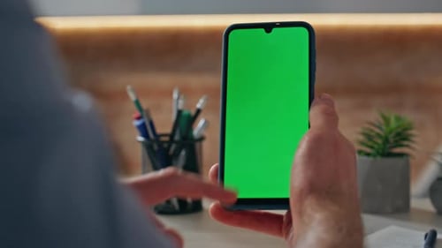 Person Taps Phone with Green Screen Indoors