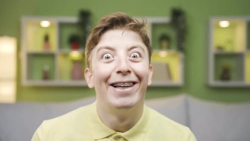 Close-up portrait of cheerful young man waving at camera.