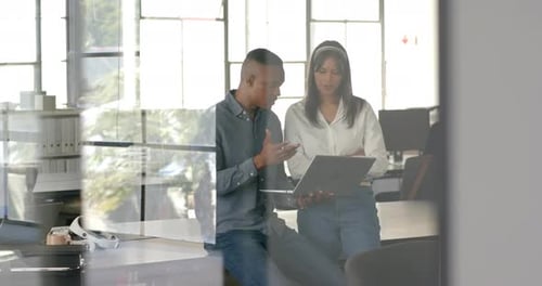 Discussing project details, colleagues using laptop in modern office setting