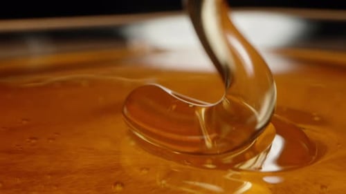 A thick trickle of honey flows spirally down, an extreme macro shot.