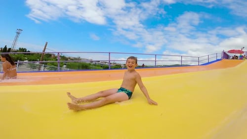 Scared and happy kid sliding in a water slide at Water Amusement Park on summer.
