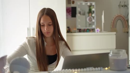 Teenage long-haired girl attending an online class and writing in her notebook at home in Vienna