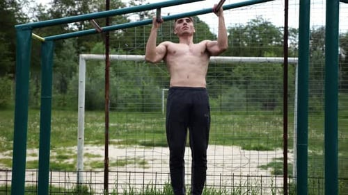 Joven deportista musculoso haciendo dominadas en un campo de deportes, un chico atlético que hace ejercicio al aire libre con fuerza