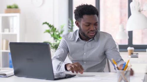 African american businessman works with laptop and financial papers in modern office