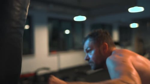 Alone Boxer is Working Out Blows on a Punching Bag in a Gym in Evening