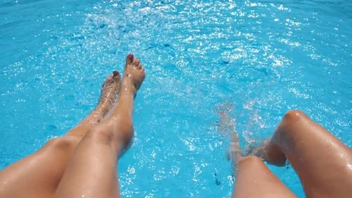 Female Legs Splashing Crystal Clear Water in Pool of Hotel Two Friends Sitting on Edge of Basin and
