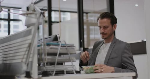 Adult male having lunch whilst working at desk in office