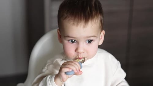 Lovely Caucasian baby boy eats himself from a special spoon for kids. Close up. High angle view.