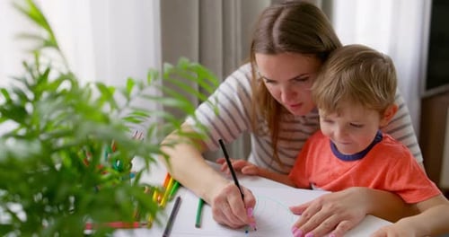 Woman and Child Drawing Together at Table Indoors
