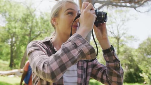 Happy diverse couple walking and taking photos in park, slow motion