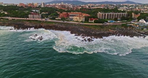 Aerial View Hugging Rocky Coast By the Sea in Cascais Portugal with Waves Crashing Underneath