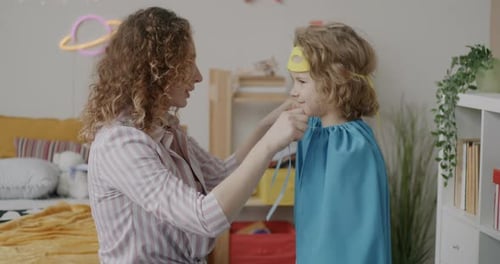 Mother Helps Child with Superhero Cape at Home