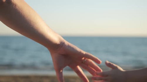 Die Hand eines Mannes nimmt die Hand eines Kindes am Meeresstrand