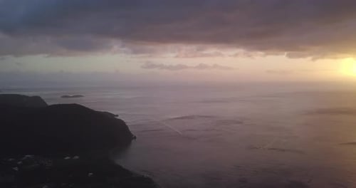Aerial view of a bay at sunset. Motor boat driving down below. Green mountain and an island in the d