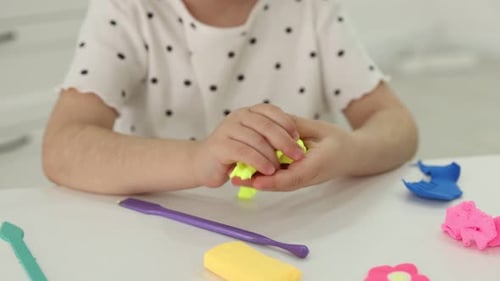 Little girl playing with colorful play dough at white table indoors, closeup