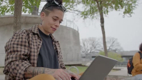 Young Female Student Using Laptop on Bench in the Park