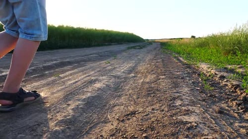 Nahaufnahme der Füße eines kleinen Jungen in Sandalen, der auf dem Weg über das Feld läuft, glückliches Kind beim Joggen