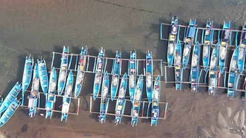 Vista aérea plana desde arriba de un gran grupo de pescadores. Los barcos azules están atracados en un muelle en Pantai Baron.