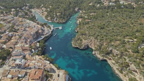 An aerial view of a picturesque Mediterranean coastal town with terracotta-roofed houses lining a vi