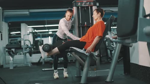 Senior Woman Exercising with Personal Trainer on Leg Extension Machine