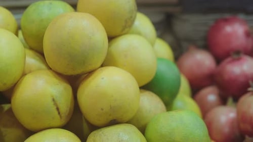 Yellow and green fruits stacked together in a market scene, with pomegranates in the background