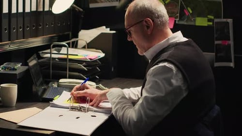 Man Reviews Documents at Desk in Dark Office