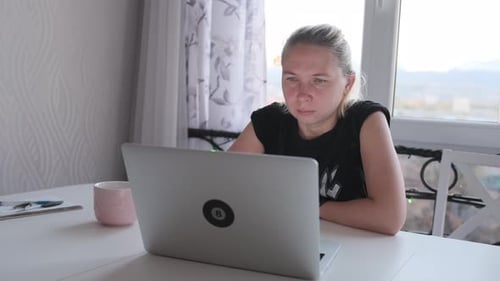 Young woman freelancer sitting at a laptop near the window close up. Distant workday concept.