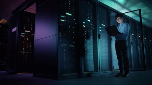 In Data Center: Male IT Technician Running Maintenance Programme on a Laptop, Controls Operational