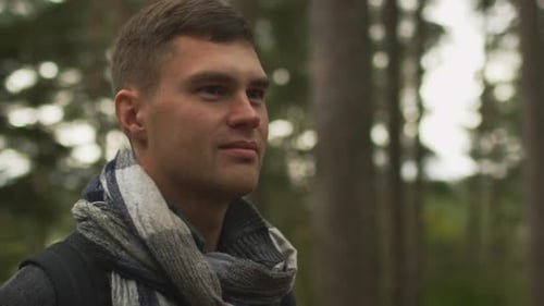 Kurzhaariger Mann in dunklem Herbstmantel und Schal steht in einem Wald und schaut sich um.