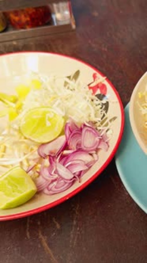 Vídeo vertical. Adicionando manualmente repolho fresco e limão à sopa tailandesa de Khao Soi com caldo de curry vermelho
e