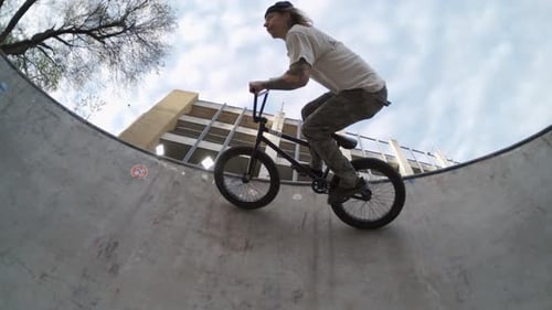 BMX biker riding sideways along the top of skatepark bowl in 800fps extreme slow-motion, sunrise fis