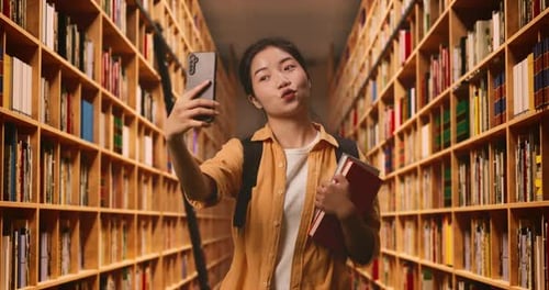Student With A Backpack And Some Books Taking Photo On Smartphone While Standing In The Library