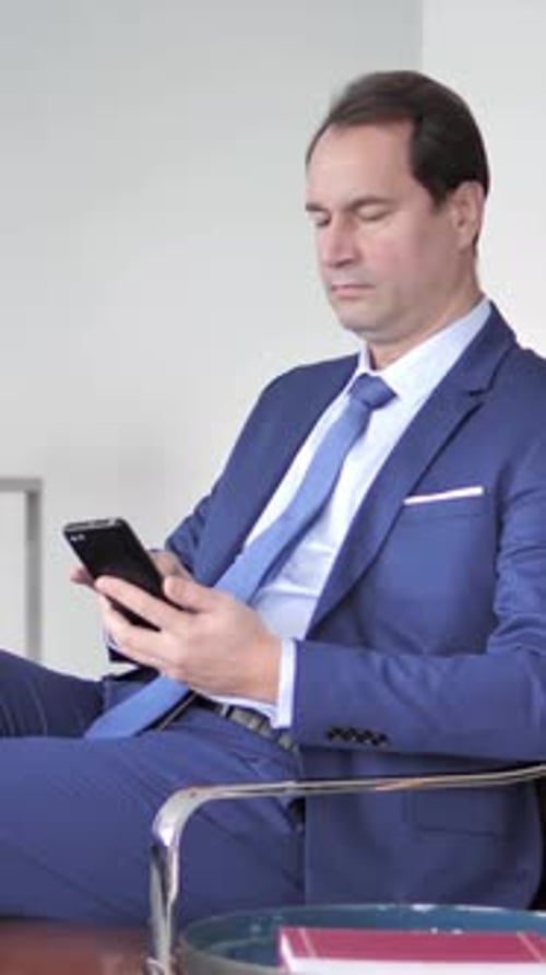 Well-Dressed Man Sits and Uses Cellphone Inside