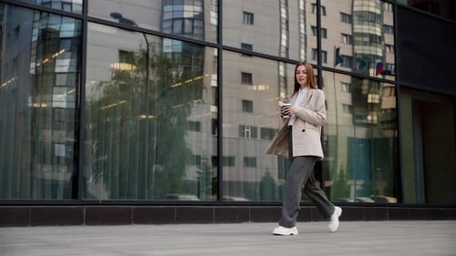 Confident Woman Walks With Coffee Past Office Building