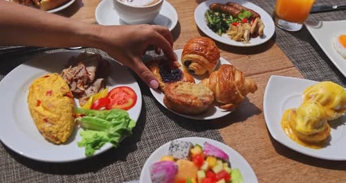 Woman reaching for pastry at luxury hotel breakfast buffet table