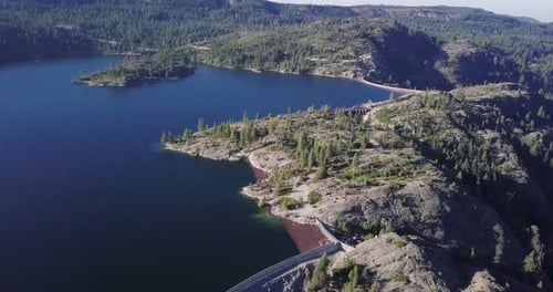 Lake with blue water surrounded by rocky Mountains pine trees redwood fly left