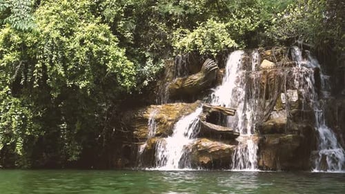 Tagsüber kleiner Wasserfall in der Natur, Blick in die Nähe der Wasseroberfläche, großer Baum steht in der Nähe