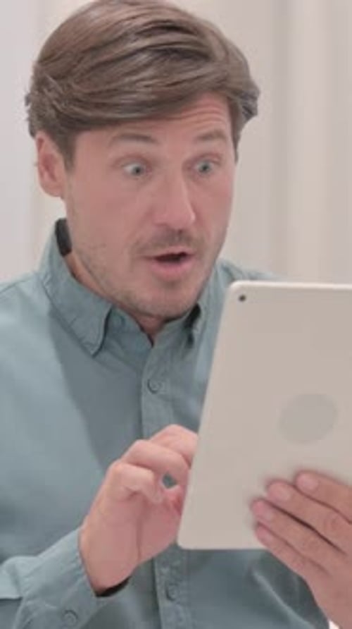 Man Looks at Tablet and Reacts with Excitement