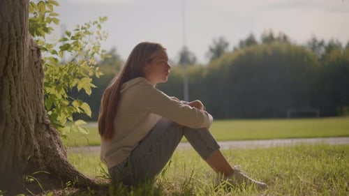 Thoughtful Woman Seated on Grassy Field with Sunlight and Peaceful Background